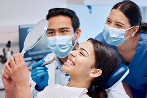 Woman smiling at reflection with dentist and dental assistant