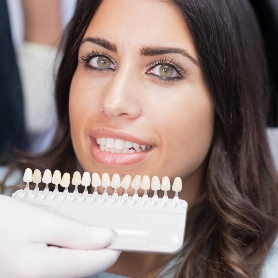 Woman in dental chair with dentist holding row of veneers to her smile