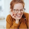 Young woman in glasses and orange sweater laughing