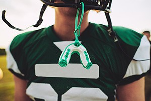 Green and white mouthguard hanging from football player's helmet