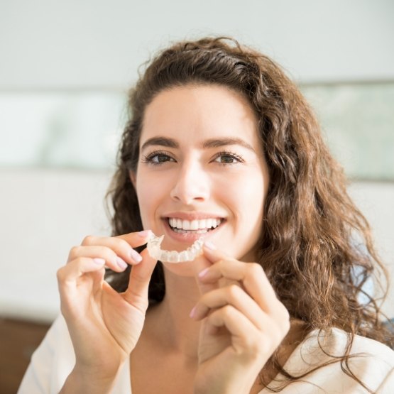 Smiling woman holding an Invisalign tray near her mouth