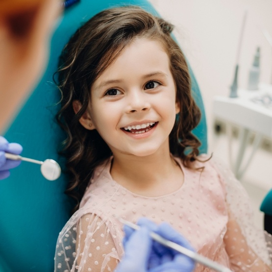 Young girl in dental chair smiling at her dentist